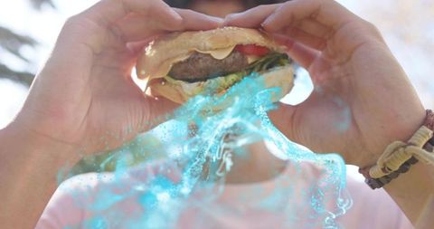 Adult wearing pink tee lifting sesame burger to mouth with neon cyan liquid effect