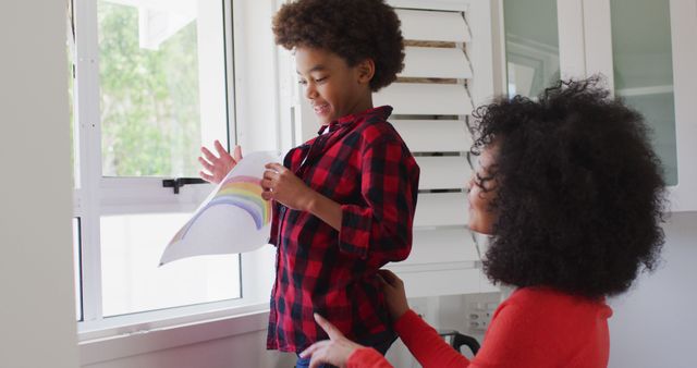 Mother Encouraging Son Holding Rainbow Drawing in Kitchen - Download Free Stock Images Pikwizard.com