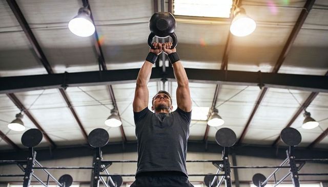 Male athlete lifting heavy kettlebell overhead industrial gym strength training wrist wraps