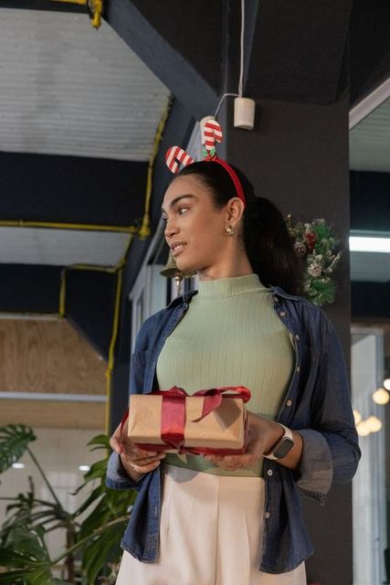 Woman standing holding holiday gift in office wearing candy cane headband and smartwatch