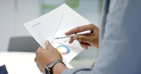 African American Professional Analyzing Growth Charts with Pen, Pointing at Rising Data