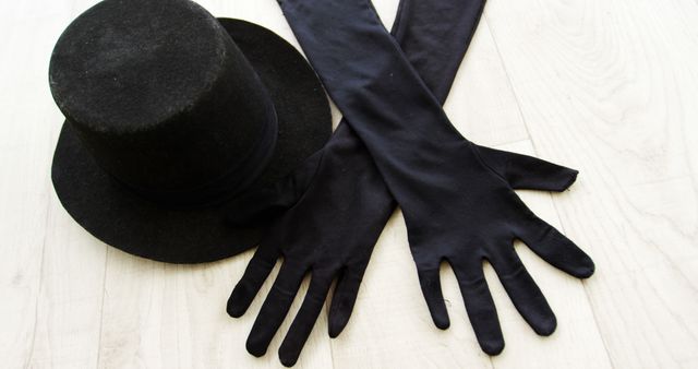 Black top hat and long black gloves placed on a light wooden surface, exuding a sense of elegance and vintage charm. Useful as a fashion accessory image for marketing, themed events, costume parties, or promotional materials for vintage clothing stores.