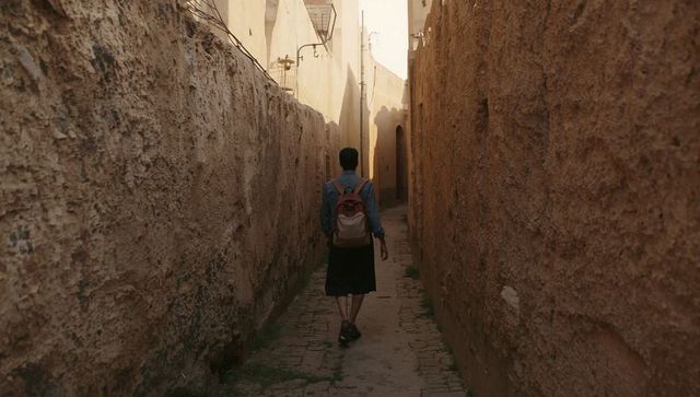 Traveler walking narrow sunlit medina alley carrying backpack on cobblestone path