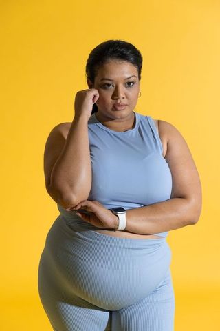Indian woman posing in blue activewear on yellow background promoting body positive fitness