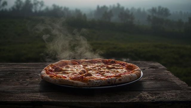 Steaming pepperoni pizza resting on weathered wooden table in misty countryside dawn