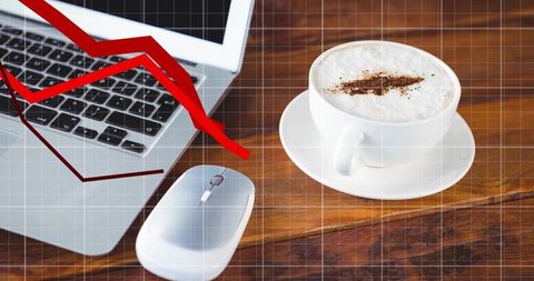 Cappuccino on wood desk beside laptop and mouse with red declining graph overlay