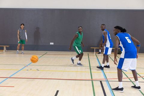 Competing basketball game with diverse players chasing ball in green and blue jerseys