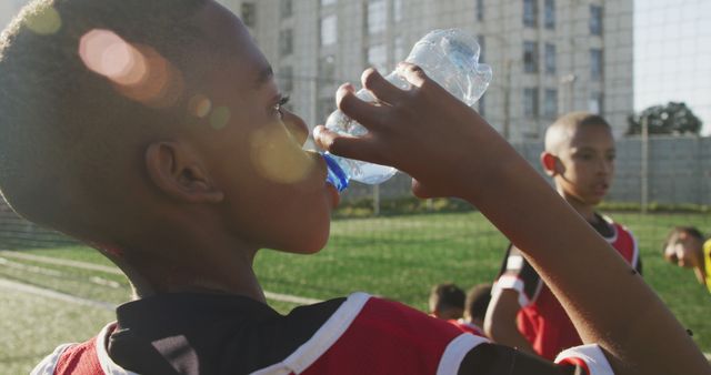 Boy in soccer uniform drinking from water bottle during outdoor practice. Perfect for content on youth sports, fitness, hydration, healthy habits, and teamwork.