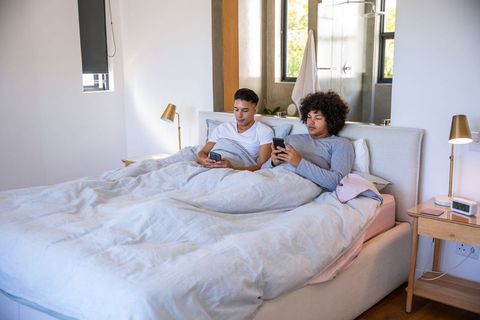 Diverse Couple Relaxing in Modern Bedroom Using Smartphones