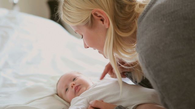 This video captures a tender moment between a mother and her baby as they bond on a bed. The mother's gentle interaction with her energetic baby, who is moving his arms and legs, conveys affection and love. This video is ideal for use in materials involving parenting, family connection, child care, and early childhood development.