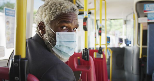 African american senior man wearing face mask travelling in the bus. hygiene and social distancing during coronavirus covid-19 pandemic.
