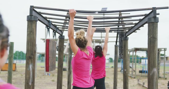 Caucasian women in pink t shirts hanging from monkey bars on bootcamp training course. Female fitness, challenge and healthy lifestyle.