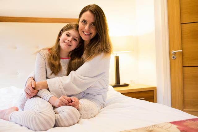 Happy mother embracing daughter in bedroom at home