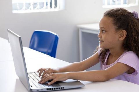 Schoolgirl typing on laptop in classroom learning digital skills and online study