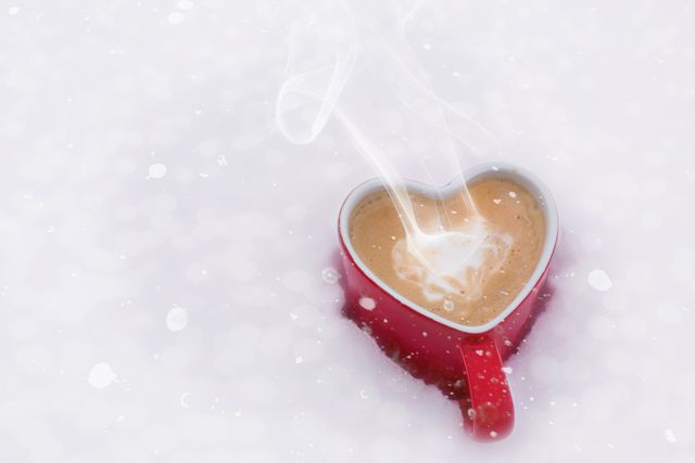 Heart shaped mug filled with steaming hot cocoa placed on snow, creating a cozy and warm feeling in a cold winter scene. Ideal for holiday greeting cards, winter-themed marketing materials, beverage promotions, or romantic winter imagery.