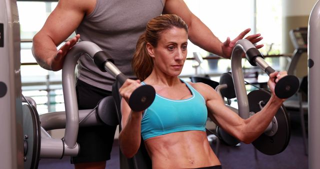 Fit woman using weights machine for arms with her trainer at the gym