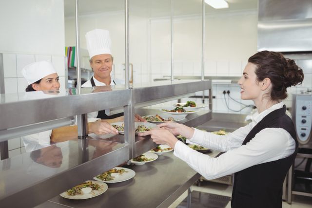 Chef handing food dish to waitress at order station - Download Free Stock Photos Pikwizard.com
