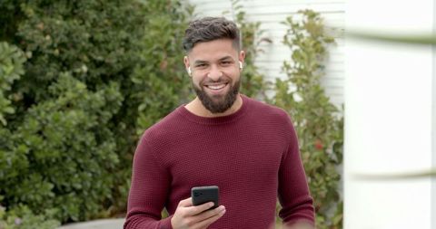 Smiling man with smartphone and earbuds in sunny garden