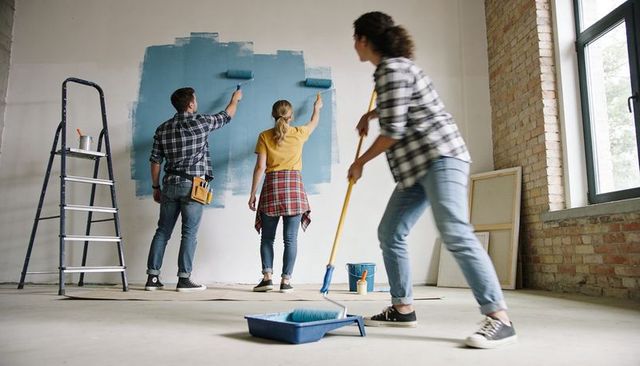 Young adults painting blue accent wall in loft renovating together diy teamwork interior