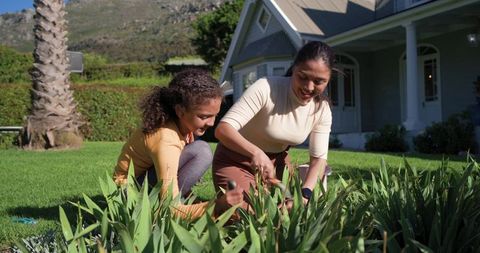 Mother and daughter gardening together in sunny suburban front yard, planting and pruning