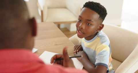African american boy getting homework help at home table with caring mentor