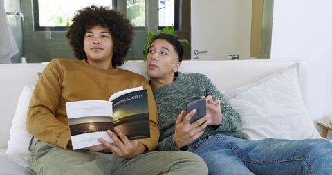 Diverse Male Partners Relaxing with Magazine and Smartphone at Home