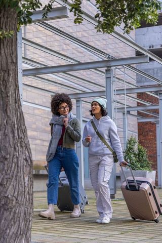 Diverse women walking, talking and pulling suitcases through urban plaza under canopy