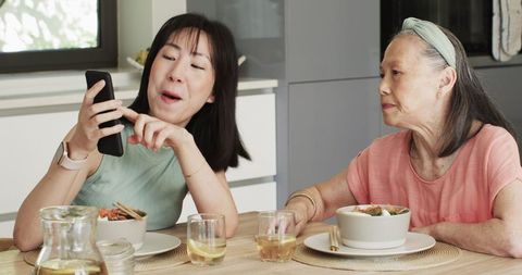 Asian grandmother and granddaughter bonding over technology at kitchen table