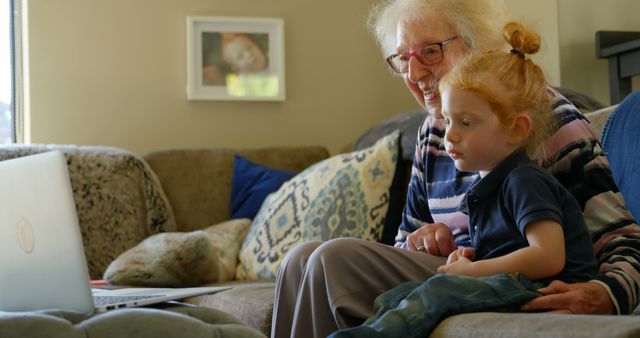 Elderly woman and young girl using laptop to video chat at home. Perfect for illustrating generational bonding, family connections, technological use by different generations, and maintaining relationships remotely. This image is ideal for articles or advertisements focusing on family tech use, video calling apps, or intergenerational relationships.