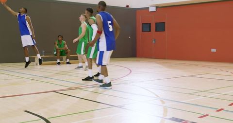 African american player leaping for layup while teammates and opponents defending on gym court