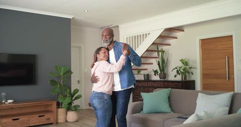 Mature diverse couple dancing at home in cozy modern living room showing affection