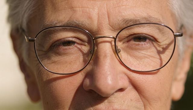 Sunlit close-up showing senior man wearing thin round glasses and facial lines