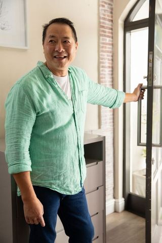 Smiling asian man welcoming at modern home entry door