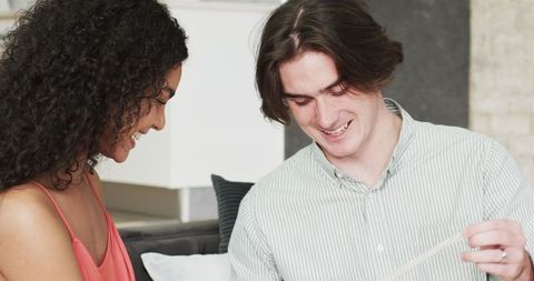 Multiracial couple surprising each other with gifts in living room celebration