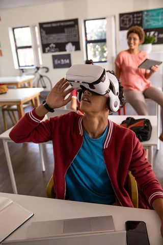 African American teacher guiding student exploring VR headset in modern classroom