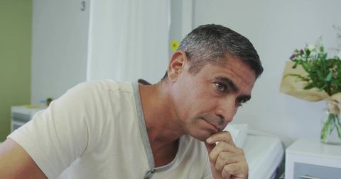 Middle-Aged Man Leaning and Resting Chin on Hand in Clinic Room Conveying Thoughtful Calm