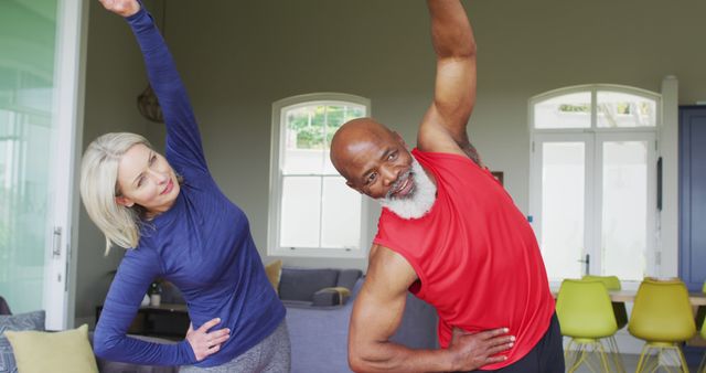 Senior couple enjoying a morning exercise routine together in their living room. Ideal for promoting articles on healthy lifestyles for seniors, fitness routines for older adults, or indoor workout guides. This image showcases themes of active living, companionship, and wellness.