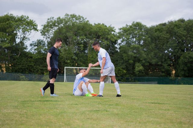 Football player assisting his friend to get up in ground