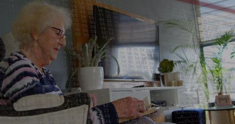 Senior woman reading book at home inside digital interface concept