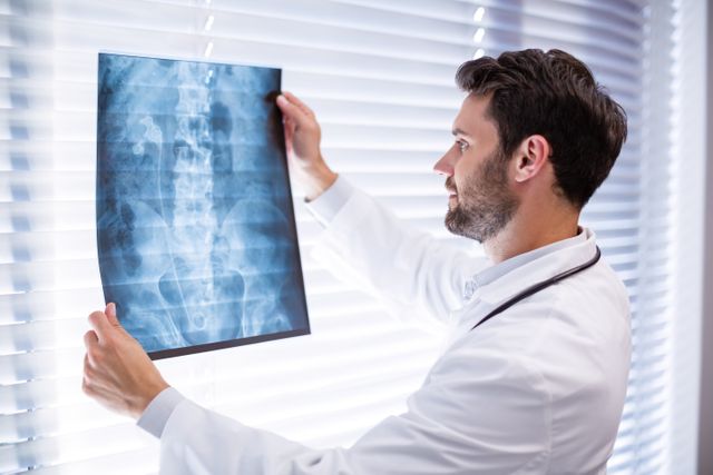 Male doctor holding and analyzing x-ray image in bright, modern clinic. Medical professional reviewing patient diagnostic results. Ideal for use in medical, healthcare, and professional settings, as well as articles on medical technology and patient care.
