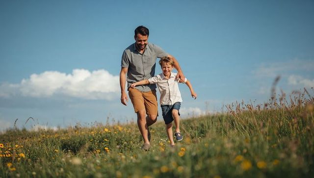 Father and son running down sunlit meadow holding hands laughing and enjoying summer bond