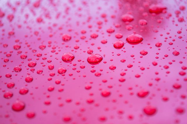 Red surface covered in water droplets forming intricate and unique patterns. Can be used for backgrounds, wallpapers, or design elements illustrating moisture, tranquility, and abstract concepts. Ideal for creative projects needing a vibrant red hue and water effect.