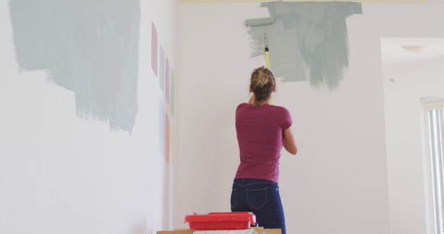 Woman in casual clothes using roller brush to paint interior wall. Ideal for articles on DIY home projects, home renovation tips, interior design, house makeovers, and step-by-step guides on painting walls.