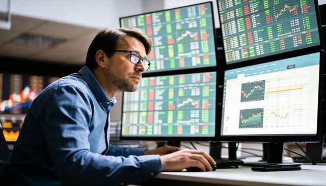 Financial analyst leaning at multi-monitor workstation analyzing real-time market charts