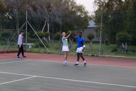 Diverse mixed-doubles tennis partners high-fiving on outdoor court celebrating teamwork