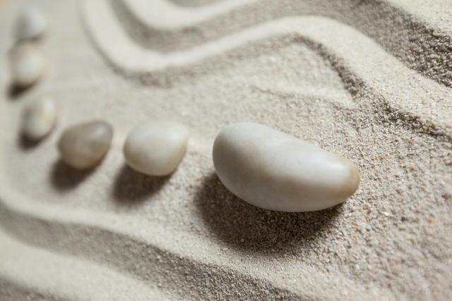 White pebble stones arranged on sand with wavy patterns, evoking a sense of tranquility and relaxation. Ideal for use in themes related to zen gardens, meditation, spa environments, and promoting a calm and peaceful atmosphere.