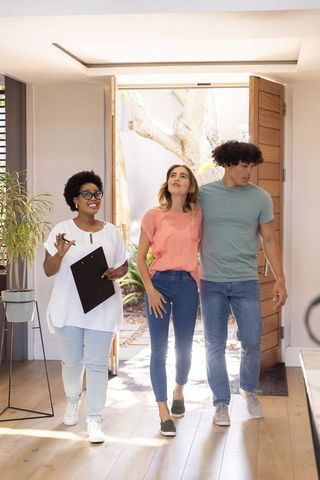 African american real estate agent guiding young couple during bright home tour in foyer