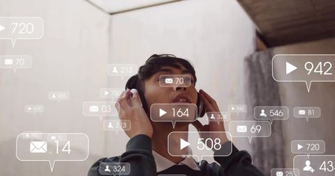 Young man listening with headphones amid floating social media notifications under skylight