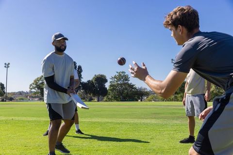 Football teammates practicing catch drill on park field boosting teamwork and fitness