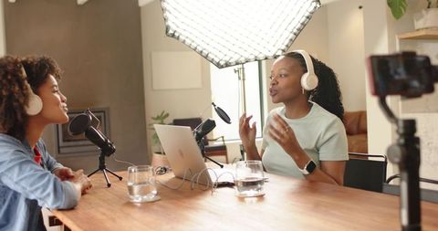 Diverse female co-hosts recording podcast with headphones and microphones in home studio
